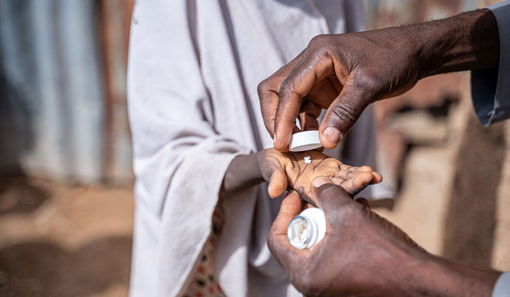 A man gives a child some tablets from a bottle as part of a Mass Drug Administration programme in Nigeria.